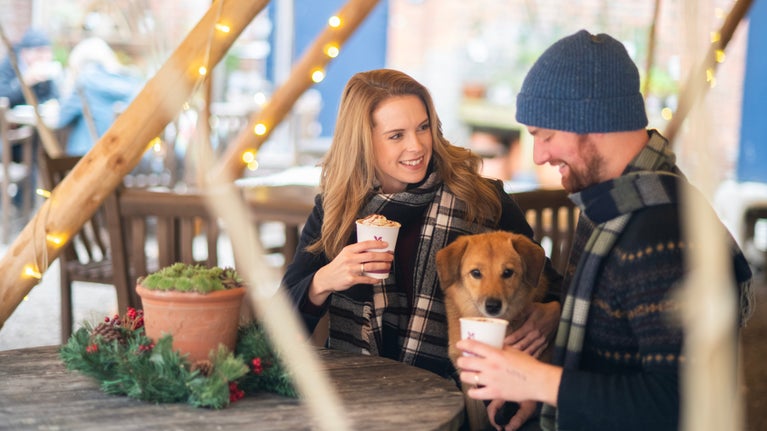 A man and woman in winter wear sat with a dog in a cafe undercover
